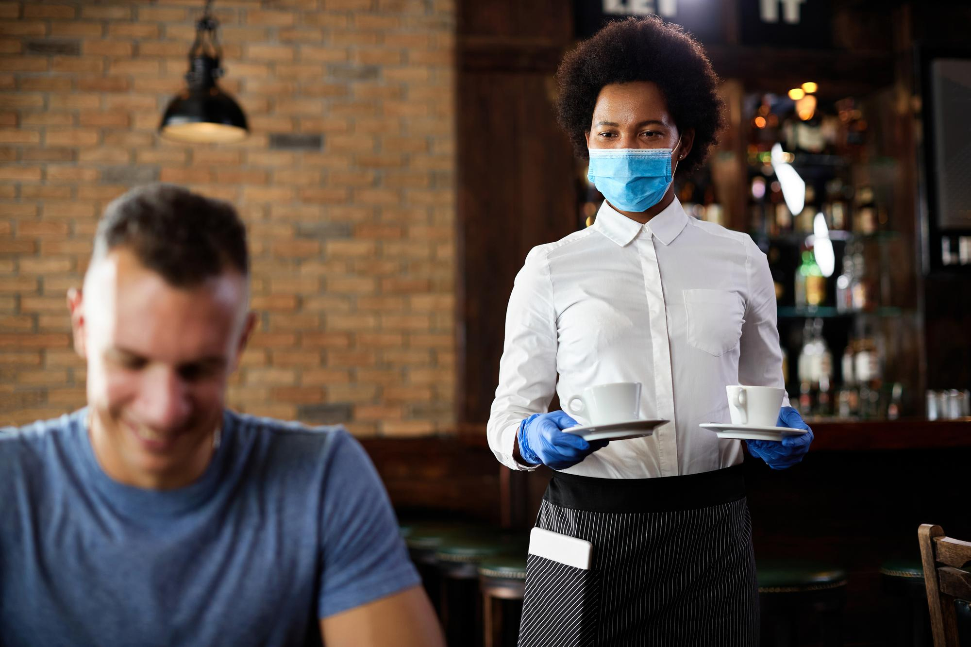 african-american-waitress-serving-coffee-while-wearing-face-mask-gloves